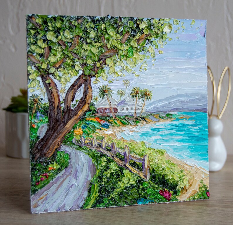 K&ouml;nnte beinhalten: Ein Gem&auml;lde, das eine tropische Strandszene mit einem gro&szlig;en gr&uuml;nen Baum im Vordergrund, einem wei&szlig;en Geb&auml;ude in der Ferne und einem blauen Meer mit Wellen zeigt. Das Gem&auml;lde ist in einem dicken, strukturierten Stil ausgef&uuml;hrt.