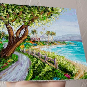 K&ouml;nnte beinhalten: Ein Gem&auml;lde, das eine tropische Strandszene mit einem gro&szlig;en Baum im Vordergrund, einem wei&szlig;en Geb&auml;ude in der Ferne und blauem Wasser mit wei&szlig;en Wellen zeigt. Das Gem&auml;lde ist in einem strukturierten Stil mit dicken Pinselstrichen ausgef&uuml;hrt.