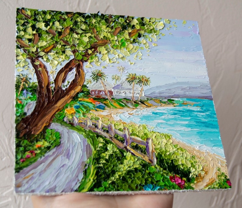 K&ouml;nnte beinhalten: Ein Gem&auml;lde, das eine tropische Strandszene mit einem gro&szlig;en Baum im Vordergrund, einem wei&szlig;en Geb&auml;ude in der Ferne und blauem Wasser mit wei&szlig;en Wellen zeigt. Das Gem&auml;lde ist in einem strukturierten Stil mit dicken Pinselstrichen ausgef&uuml;hrt.