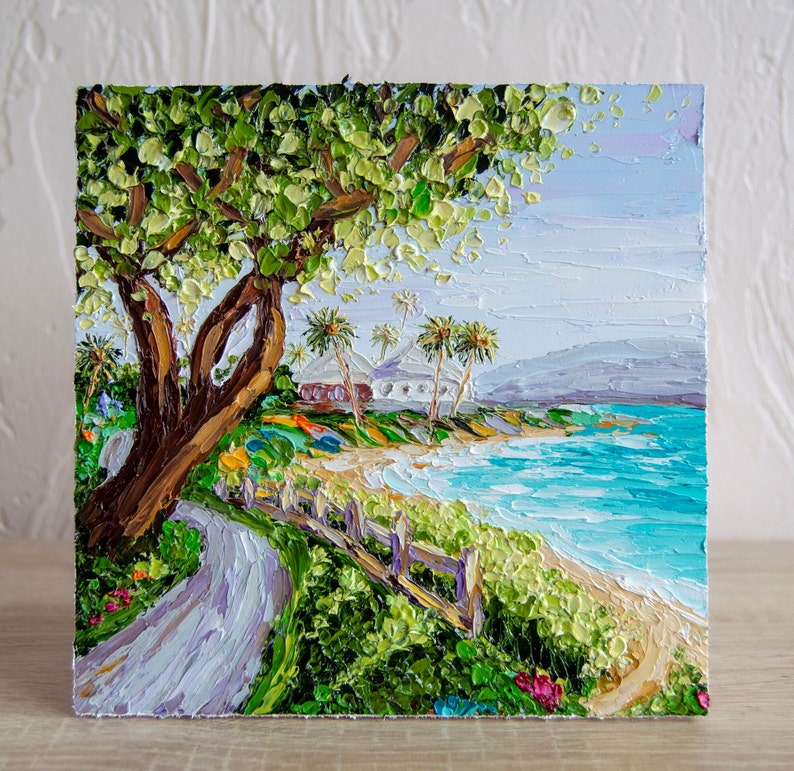 K&ouml;nnte beinhalten: Ein Gem&auml;lde, das eine Strandszene mit einem gro&szlig;en gr&uuml;nen Baum im Vordergrund, einem wei&szlig;en Geb&auml;ude in der Ferne und blauem Wasser mit wei&szlig;en Wellen zeigt.