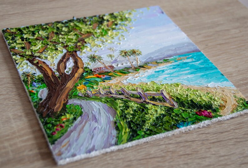 K&ouml;nnte beinhalten: Ein Gem&auml;lde, das eine Strandszene mit einem Weg zum Ufer zeigt. Der Weg ist von gr&uuml;nen B&uuml;schen und einem Holzzaun ges&auml;umt. Ein gro&szlig;er Baum mit gr&uuml;nen Bl&auml;ttern befindet sich auf der linken Seite des Gem&auml;ldes. Der Strand ist sandig mit blauem Wasser und wei&szlig;en Wellen. Der Himmel ist hellblau mit wei&szlig;en Wolken.