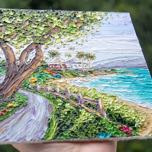 K&ouml;nnte beinhalten: Ein Gem&auml;lde, das eine Strandszene mit einem gewundenen Weg zum Ufer zeigt. Das Gem&auml;lde zeigt einen gro&szlig;en Baum mit gr&uuml;nen Bl&auml;ttern, Palmen, ein wei&szlig;es Haus und ein blaues Meer. Das Gem&auml;lde ist in einem strukturierten Stil mit dicken Pinselstrichen ausgef&uuml;hrt.