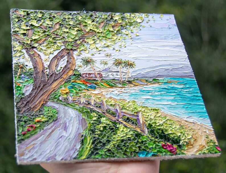 K&ouml;nnte beinhalten: Ein Gem&auml;lde, das eine Strandszene mit einem gewundenen Weg zum Ufer zeigt. Das Gem&auml;lde zeigt einen gro&szlig;en Baum mit gr&uuml;nen Bl&auml;ttern, Palmen, ein wei&szlig;es Haus und ein blaues Meer. Das Gem&auml;lde ist in einem strukturierten Stil mit dicken Pinselstrichen ausgef&uuml;hrt.