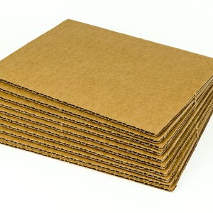 May include: A stack of brown corrugated cardboard sheets. The edges reveal the fluted interior structure of the cardboard. The sheets are rectangular and appear to be new. The stack is on a white background.