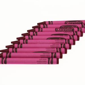 May include: A stack of Crayola crayons in the color red violet. The crayons are arranged in a fan shape with the tips of the crayons facing the viewer. The crayons are labeled "Crayola" and "red violet" in English and Spanish.