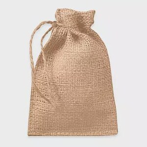 May include: A small, beige burlap drawstring bag. The bag has a woven texture and a natural, rustic appearance. The drawstring is made of a matching beige twine.