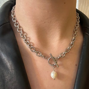 May include: A silver chain necklace with a toggle clasp and a single pearl pendant.
