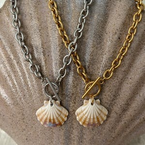 May include: Two gold and silver chain necklaces with a seashell pendant. The chains are both toggle clasps. The seashells are a light brown color.