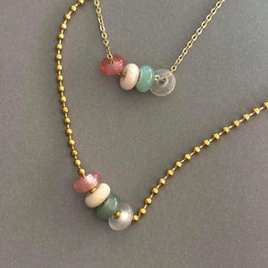 May include: Two delicate gold necklaces. One has a chain of small gold beads, the other a fine chain. Both feature colourful gemstone pendants. The pendants are made of pink, white, green, and clear circular stones.