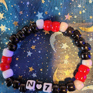 May include: Black, red, and white beaded bracelet with a charm that says "N ♥ 7".