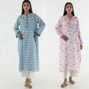 May include: Two long-sleeved dresses. One is white with a blue floral pattern, the other is pink with a floral print. Both dresses have a long, loose fit and are paired with white, eyelet-detailed pants. The models are wearing sandals.