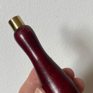 Könnte beinhalten: Ein dunkelroter Holzgriff mit einer goldenen Metallspitze. Der Griff ist glatt und poliert.