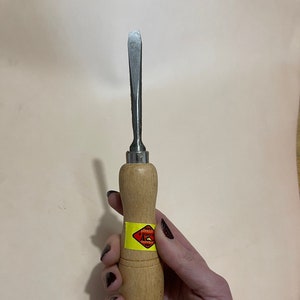 May include: A wood handled leather working tool with a metal blade. The handle has a yellow warning label with red text that reads "Danger! Keep away from children".