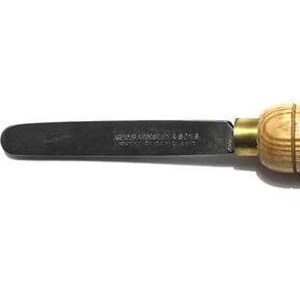 May include: A wood turning tool. It features a dark metal blade and a light-coloured wooden handle. The handle is rounded with visible wood grain. The blade is connected to the handle with a brass fitting.