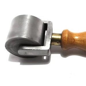 Puede incluir: Un rodillo de costura de metal con mango de madera. El rodillo es de metal plateado y tiene forma redondeada. El mango es de madera clara y está unido al rodillo con un accesorio de latón. La herramienta está diseñada para alisar costuras.