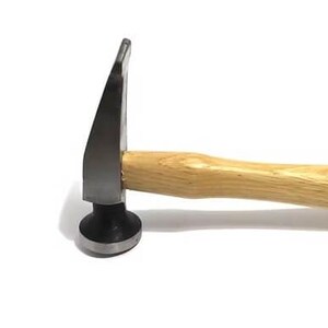 May include: A metal hammer with a wooden handle. The hammerhead is dark grey with a flat, circular striking surface and a curved, angled peen. The handle is light brown.