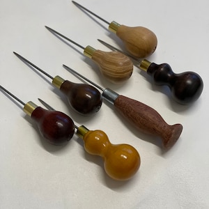May include: Six leather stitching awls with wooden handles in various colors and styles. The awls have metal tips and brass ferrules.