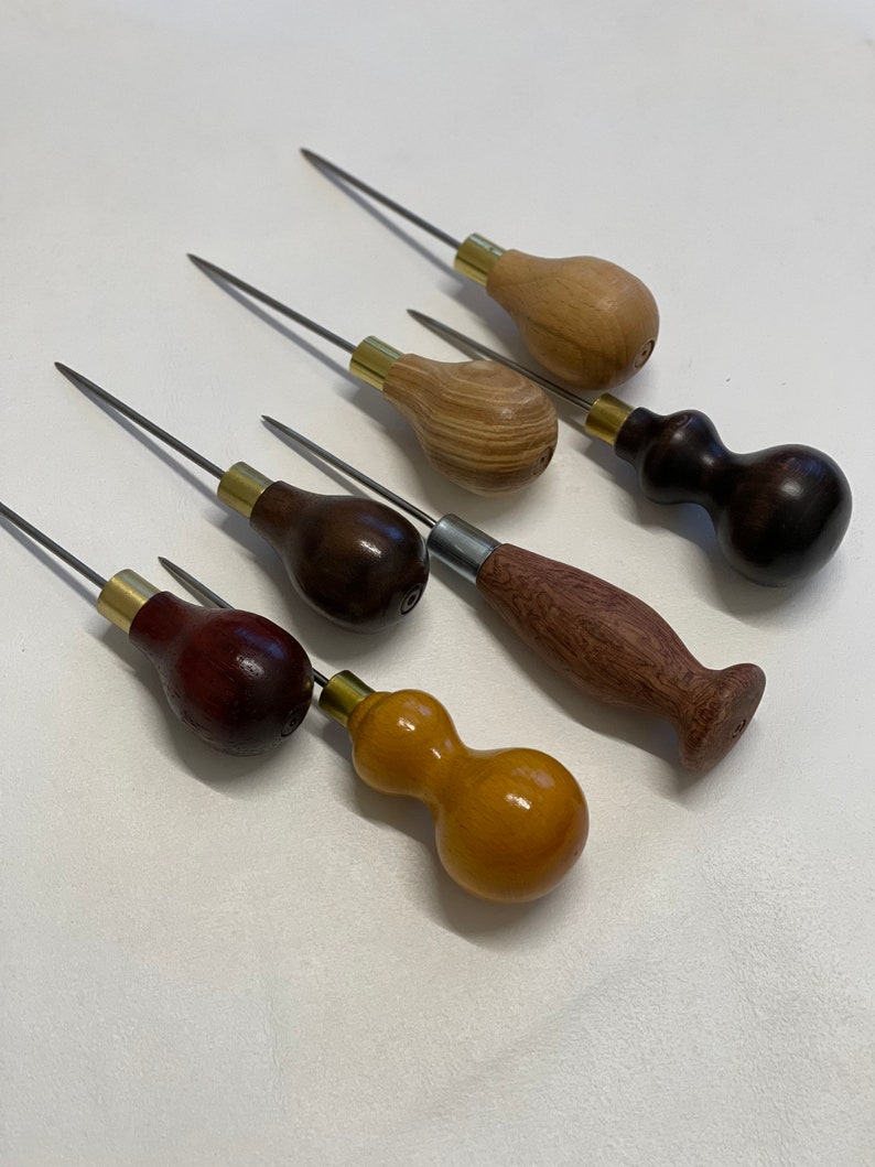 May include: Six leather stitching awls with wooden handles in various colors and styles. The awls have metal tips and brass ferrules.