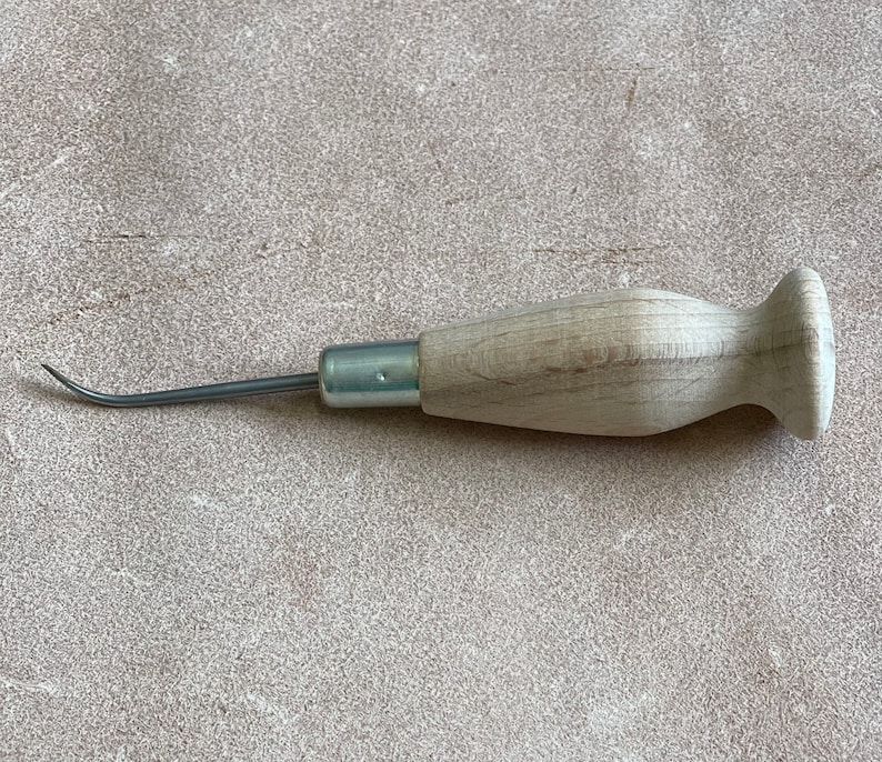 May include: A wooden-handled leather sewing awl with a curved metal needle.