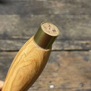Op de afbeelding: Close-up van een houten handvat met een messing top. De top heeft een kurken inzet met een klein gaatje in het midden.