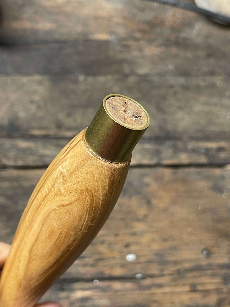 Op de afbeelding: Close-up van een houten handvat met een messing top. De top heeft een kurken inzet met een klein gaatje in het midden.