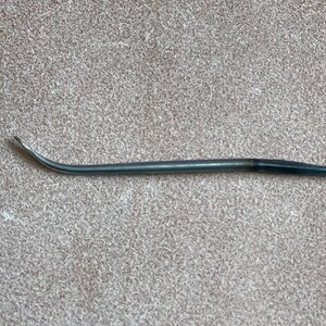 May include: A curved, silver-toned needle with a black tip. The needle is used for sewing leather.