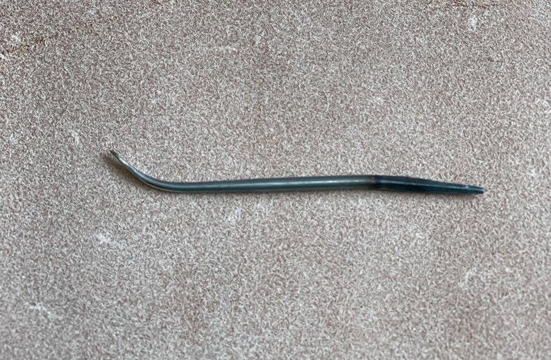 May include: A curved, silver-toned needle with a black tip. The needle is used for sewing leather.
