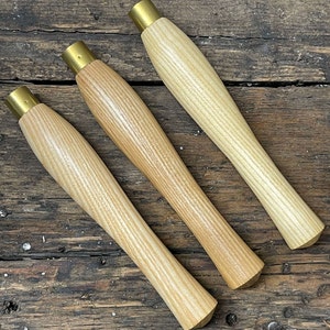 Op de afbeelding: Drie houten gereedschapsstelen met messing beslag. De stelen zijn lichtbruin en hebben een houtnerfpatroon.