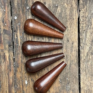 May include: Six wooden dowels with a dark brown stain. The dowels are arranged in a fan shape on a wooden surface.