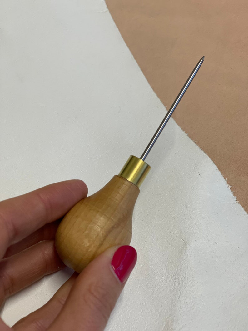 May include: A wooden-handled leather stitching awl with a brass ferrule and a sharp metal needle.