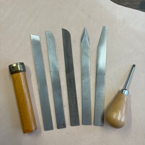 Puede incluir: Un conjunto de siete herramientas para trabajar el cuero, que incluye un punzón de costura con mango de madera y seis tipos diferentes de cuchillos para desbastar cuero.