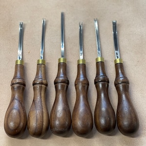 Può includere: Sei strumenti per la lavorazione del cuoio con manici in legno. Gli strumenti sono numerati da 0 a 5 e hanno una lama argentata.