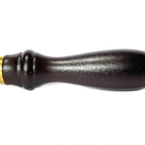 May include: A dark brown wooden handle with a gold metal cap. The handle is smooth and has a slight curve. It is a replacement handle for a tool or implement.