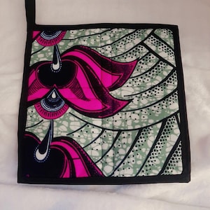 Puede incluir: Manopla de cocina cuadrada acolchada con borde y lazo para colgar negros. La tela presenta un vibrante estampado de formas florales rosas y negras sobre un fondo verde claro con lunares blancos. Para la cocina.