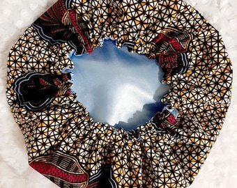 Könnte beinhalten: Eine satin-gefütterte Haarbürste mit einem geometrischen Muster in Gelb-, Braun- und Weißtönen. Die Bürste hat ein blaues und rotes Blumenmuster an der Seite.