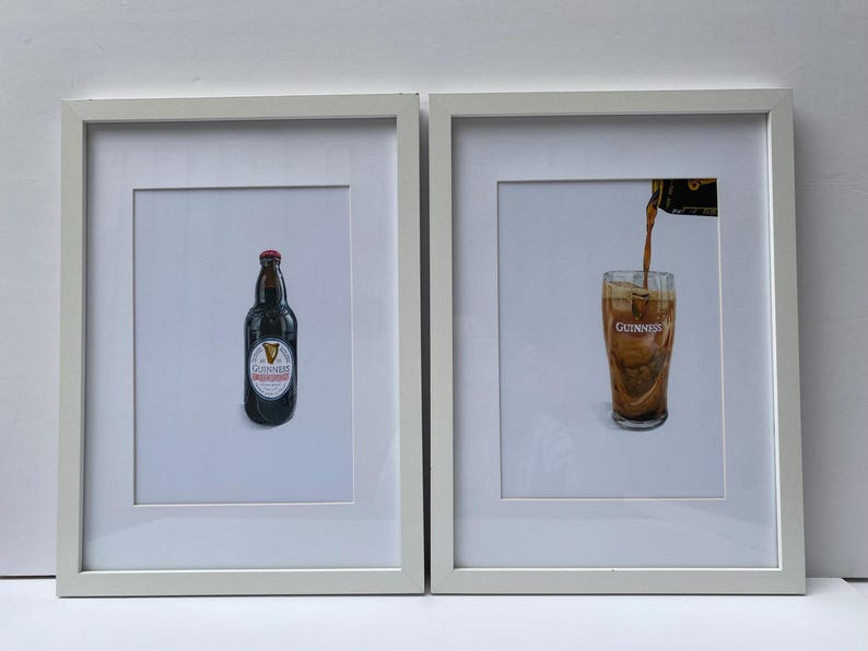 May include: Two framed prints featuring Guinness beer. One print shows a bottle of Guinness with a red cap and a white label. The other print depicts beer being poured into a glass, with the Guinness logo visible.