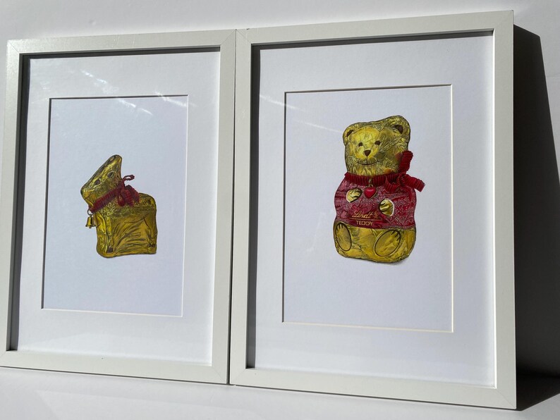 Puede incluir: Dos impresiones enmarcadas con figuras de chocolate envueltas en papel dorado. Una impresi&oacute;n muestra un conejito envuelto con una cinta roja y una campana. La otra impresi&oacute;n representa un oso de peluche con un su&eacute;ter rojo con un coraz&oacute;n.