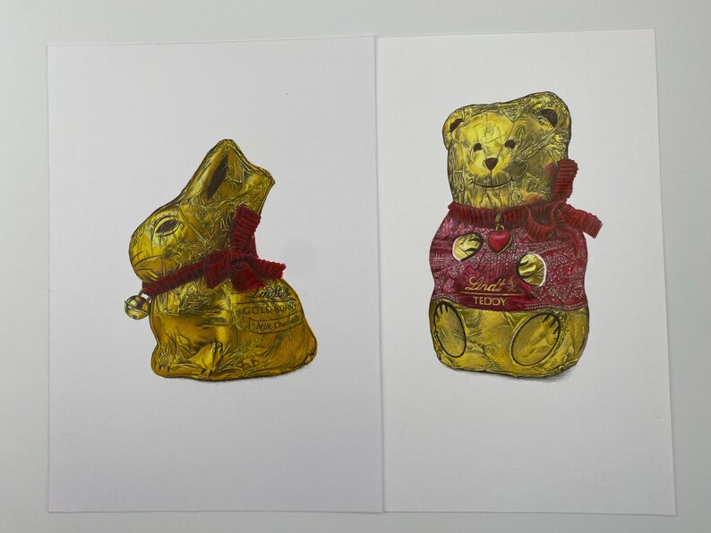 Puede incluir: Dos figuras de chocolate envueltas en papel dorado: un conejito dorado con lazo y campana rojos, y un osito dorado con un su&eacute;ter rojo con un coraz&oacute;n. El oso tiene el texto "Lindt TEDDY".