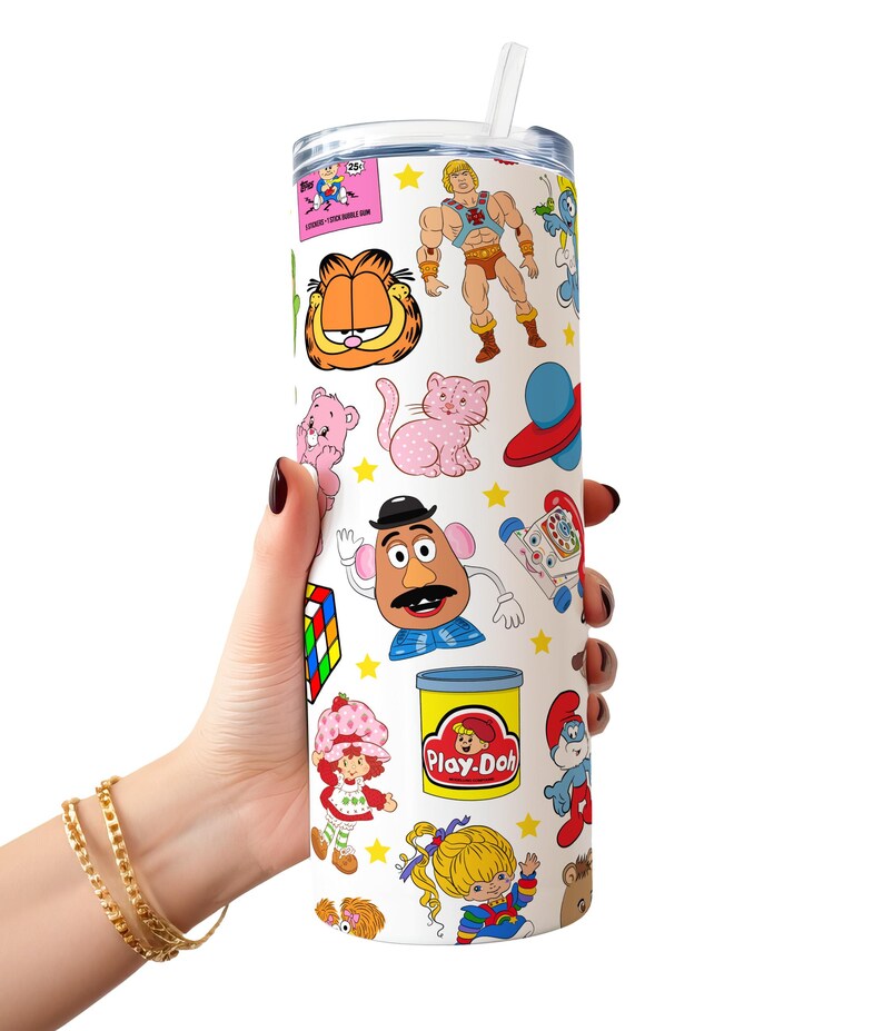 May include: A white tumbler with a straw, featuring a colourful pattern of 80s cartoon characters, including Garfield, He-Man, Care Bears, Strawberry Shortcake, and Play-Doh.