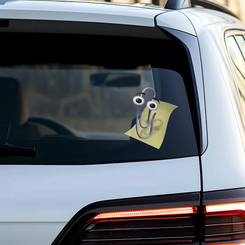 May include: A white car with a paperclip sticker on the back window. The paperclip has googly eyes and is holding a yellow sticky note.