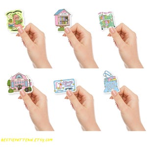 May include: A collection of colorful stickers featuring library-themed designs. The stickers include a library bookworm, a pink library building, a library cart, a library card, and a bag of books. The stickers are held in hands.