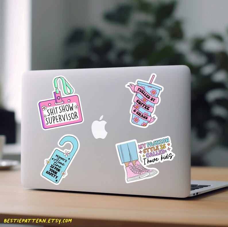 May include: Four colorful stickers on a silver laptop. The stickers feature humorous sayings about coffee, fashion, and motherhood. The stickers are pink, blue, and green with white text.