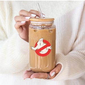 May include: A clear glass reusable iced coffee cup with a bamboo lid and a straw. The cup has a graphic of a ghost with a red circle and slash through it.