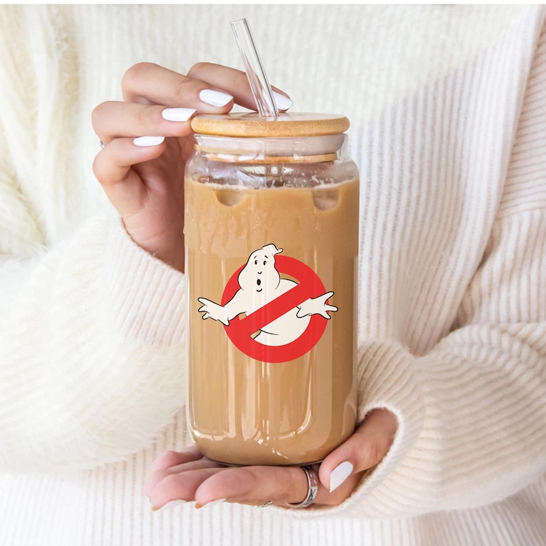 May include: A clear glass reusable iced coffee cup with a bamboo lid and a straw. The cup has a graphic of a ghost with a red circle and slash through it.
