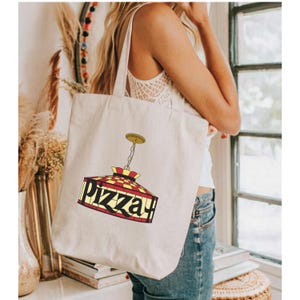 May include: A white canvas tote bag featuring a red, yellow and black checkered light fixture design. The light fixture has the word "Pizza" written on it.