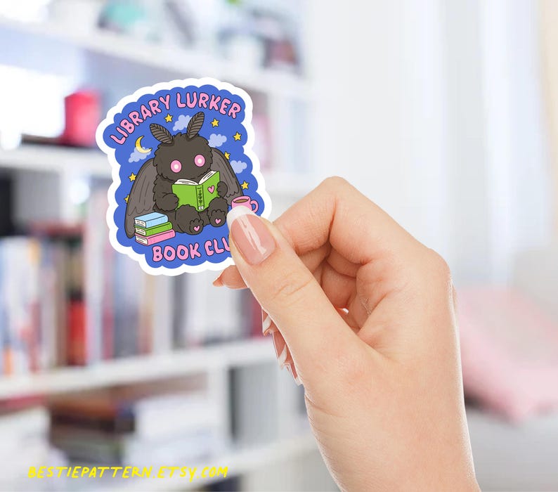 May include: A sticker featuring a cartoon moth reading a book, with the text "LIBRARY LURKER BOOK CLUB". The moth is black with pink eyes and is holding a green book. A pink mug and a stack of books are also visible.