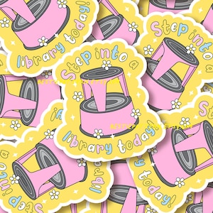 May include: A collection of stickers with a pink step stool design. The stickers have a yellow background with the text "Step into a library today!" in a playful font, and small white flower accents.
