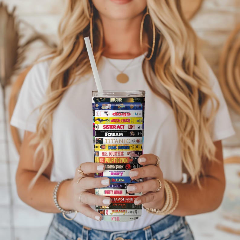 May include: A stainless steel tumbler with a colorful design featuring the titles of popular movies. The tumbler is wrapped with a design that looks like VHS tapes. The titles include "Reservoir Dogs", "Sister Act", "Scream", "Titanic", "Mrs. Doubtfire", "Pulp Fiction", "Jurassic Park", "The Matrix", "Pretty Woman", "Shawshank Redemption", "Seven", "My Girl", and more.