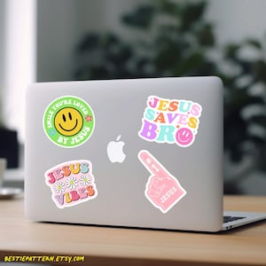 Puede incluir: Un ordenador port&aacute;til con cinco pegatinas coloridas. Las pegatinas muestran una cara sonriente con el texto "Smile You're Loved By Jesus", una mano con el texto "#1 Jesus", el texto "Jesus Saves Bro" y el texto "Jesus Vibes" con margaritas.