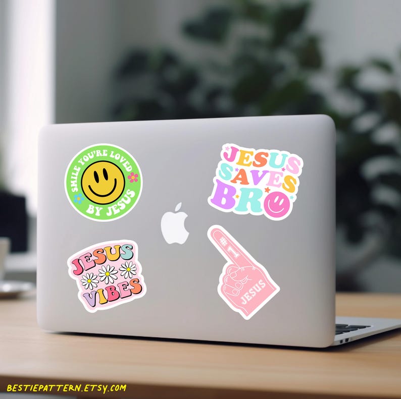 Puede incluir: Un ordenador port&aacute;til con cinco pegatinas coloridas. Las pegatinas muestran una cara sonriente con el texto "Smile You're Loved By Jesus", una mano con el texto "#1 Jesus", el texto "Jesus Saves Bro" y el texto "Jesus Vibes" con margaritas.